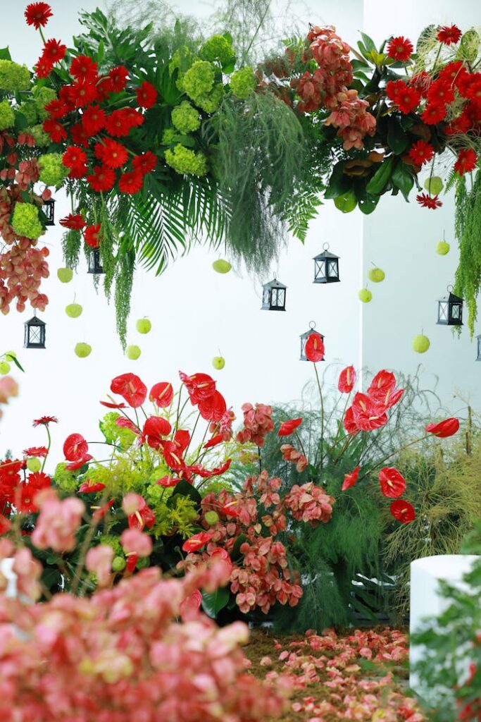 Lush red and green floral arrangement with decorative lanterns in an indoor space.